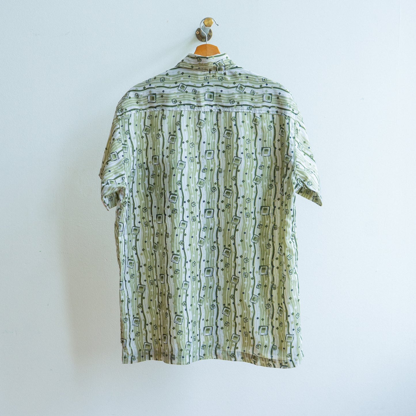 Green patterned vintage shirt from the 90s in white and khaki with short sleeves with an underground look on a hanger