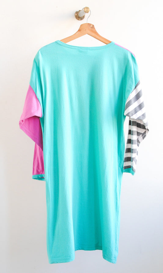 Back of a long vintage tshirt in baby blue with one pink sleeve and one black and white striped sleeve from the 1980s on a hanger