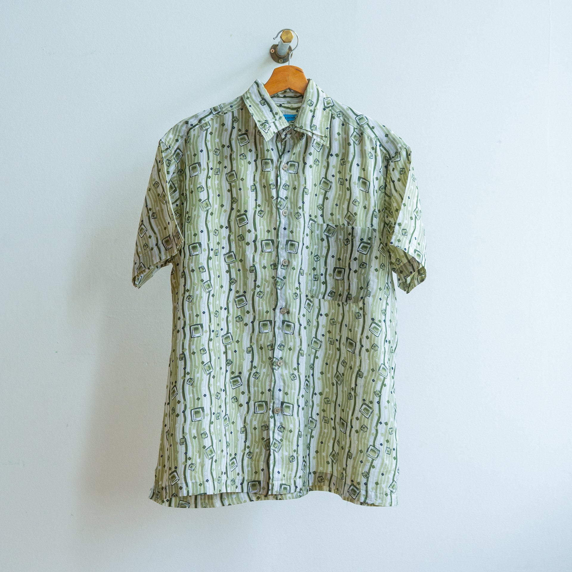 Short-sleeve vintage shirt from the 90s in white and khaki with abstract pattern of lines and squares for an underground look on a hanger