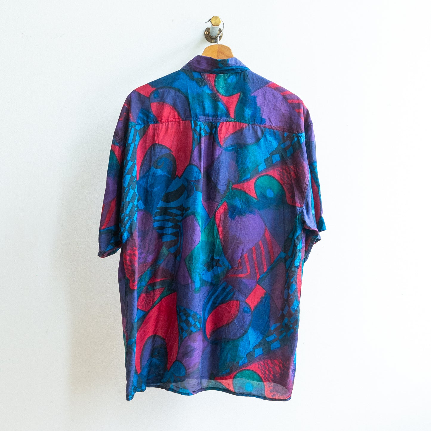 back of a colorful patterned abstract vintage shirt in dark blue purple green red in a soft fabric on a hanger