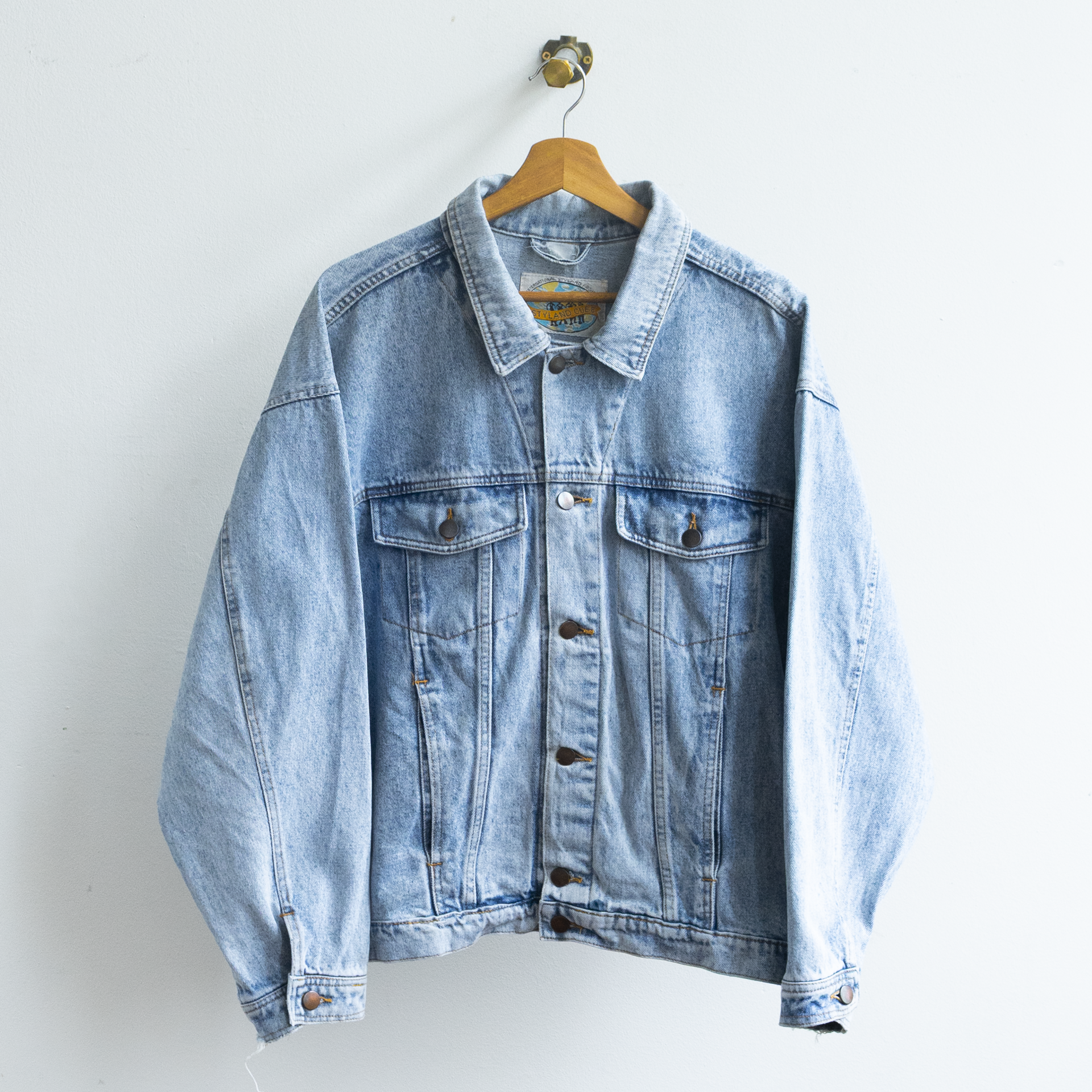 A light wash vintage 90s blue denim jacket hanging on a wooden hanger against a plain white wall