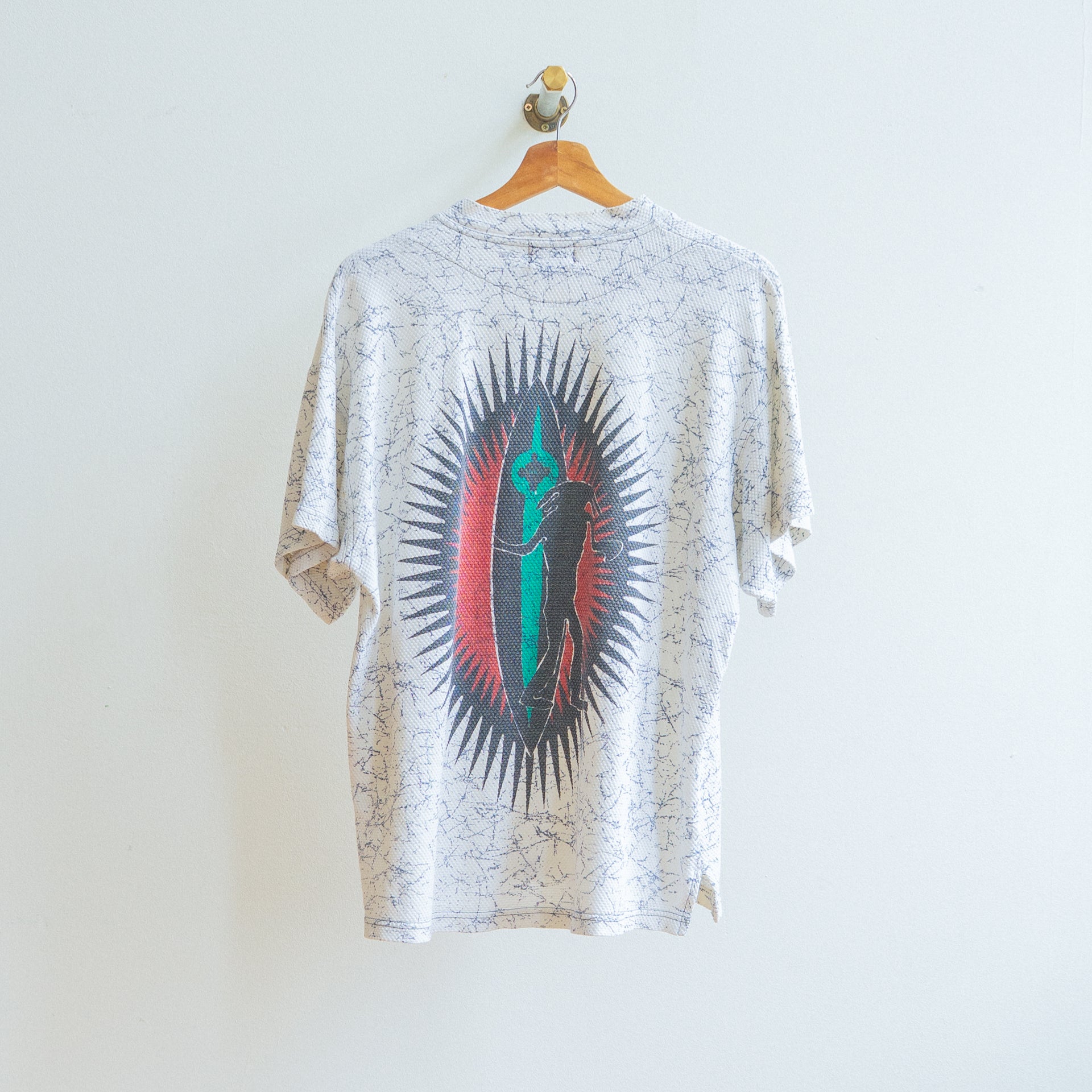 witte jaren 80 vintage tshirt met blauwe krakelingen met design van een cartoon die een surfbord vastheeft in rood-zwarte cirkel met zonnestralen aan de achterkant