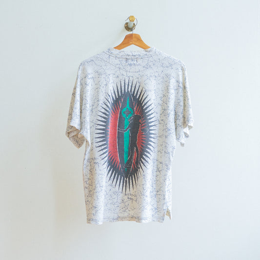 witte jaren 80 vintage tshirt met blauwe krakelingen met design van een cartoon die een surfbord vastheeft in rood-zwarte cirkel met zonnestralen aan de achterkant