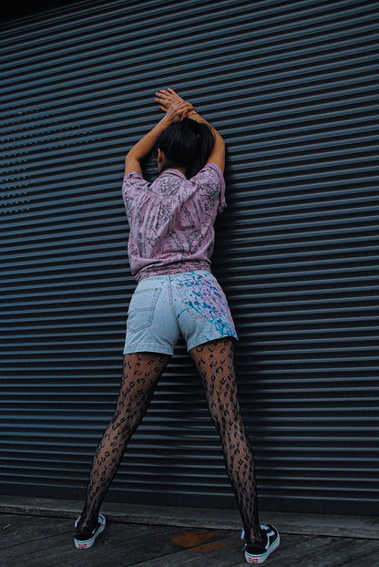model-wearing-leopard-stockings-and-light-jeans-short-with-paint-splatters-in-blue-and-pink-on-the-back-from-the-fresh-vintage-art-wear-collection-leaning-towards-garage-door
