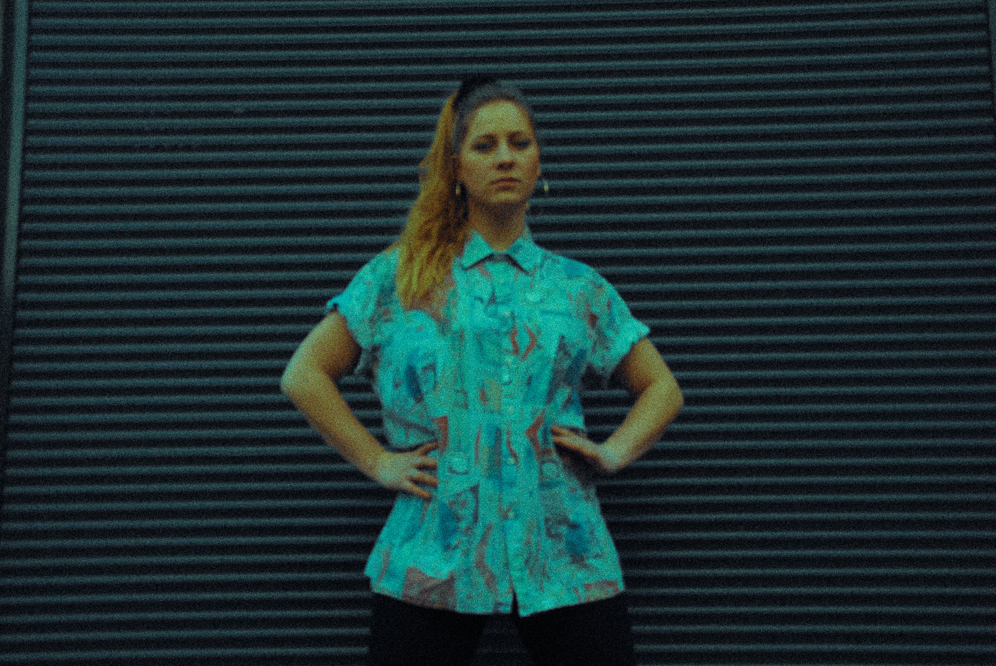 artsy picture of a young woman in front of a garage door wearing an abstract shirt and big round earrings 90s classy ghetto style 